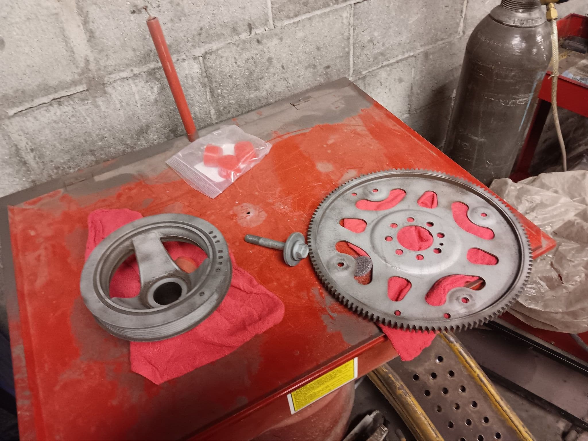 Metal gears and engine components on red workbench with tools and cleaning cloths.