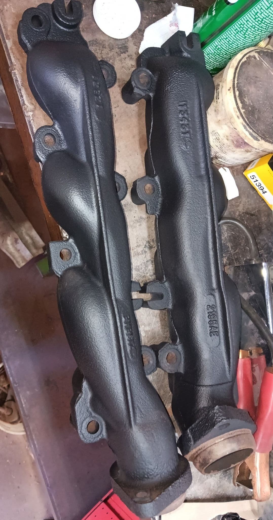 Two black automotive exhaust manifolds on a workbench, showcasing detailed design and craftsmanship.