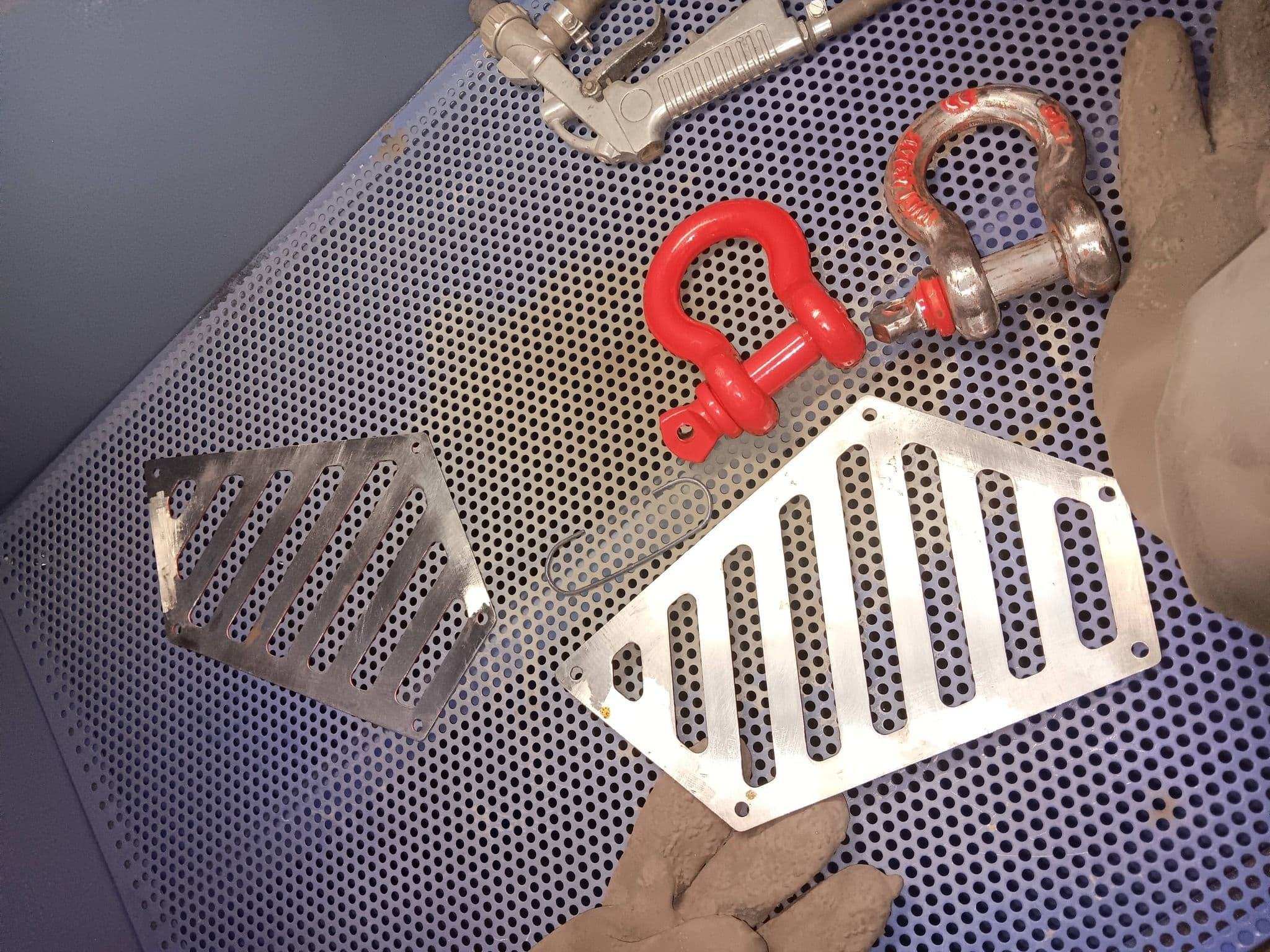 Metal plates and red shackles on a perforated surface with gloves nearby.