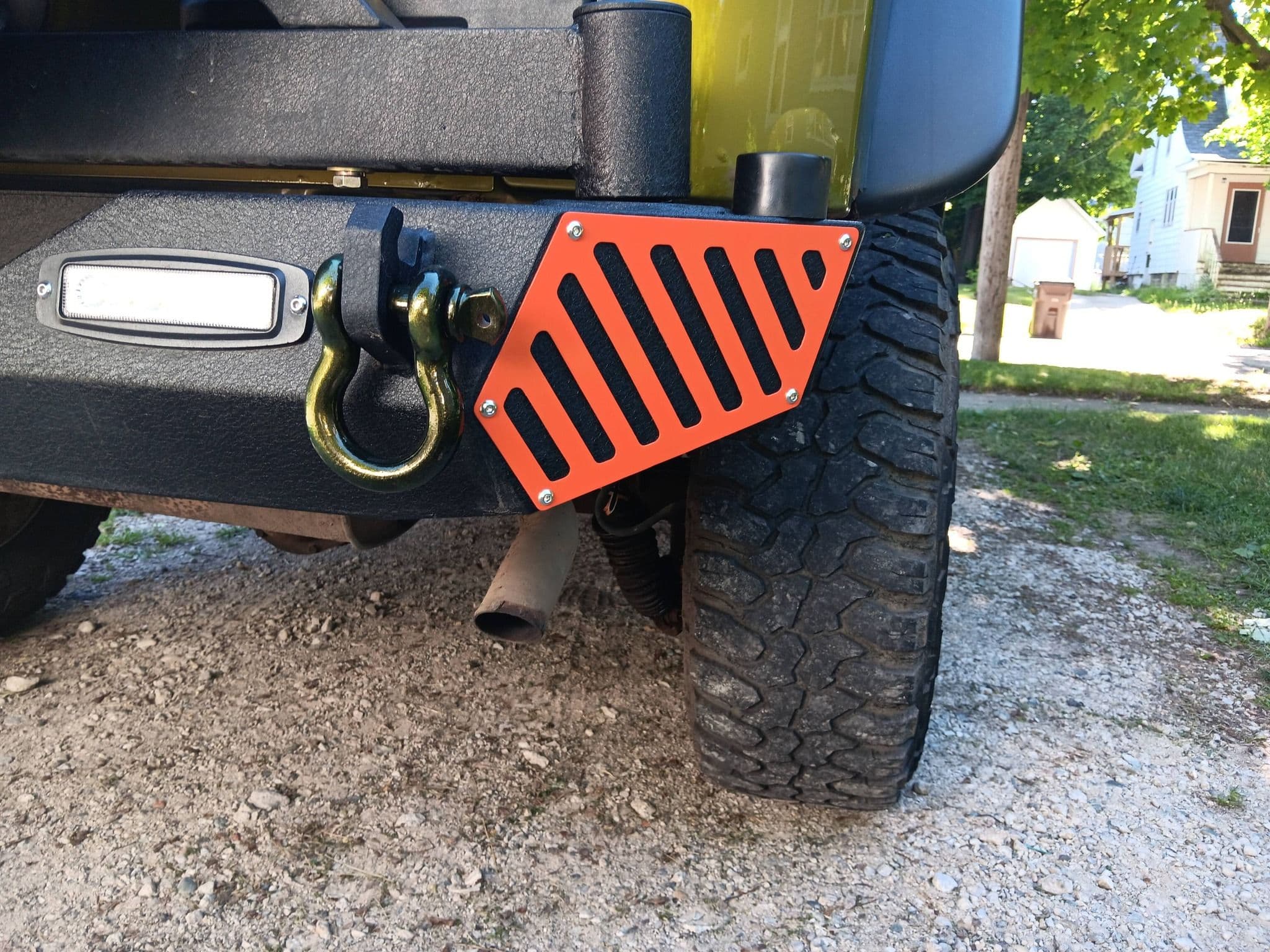 Off-road vehicle with an orange skid plate and winch attachment, parked on gravel.
